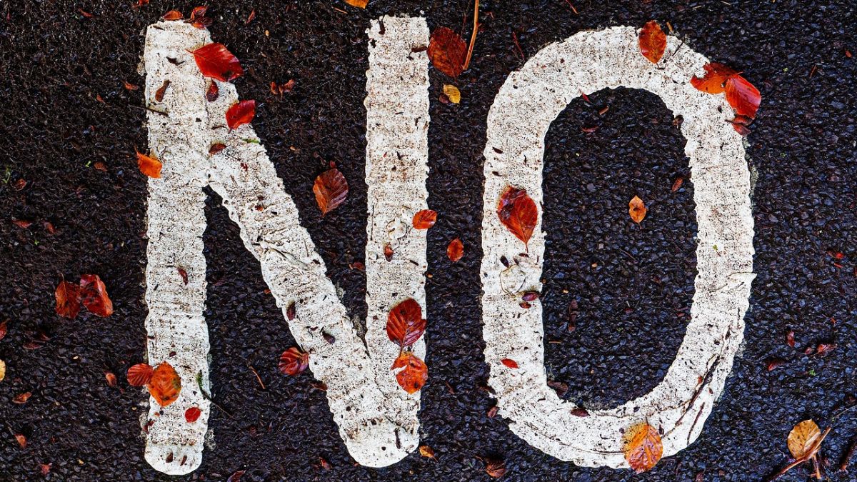 A road with fallen leaves and a 'No' sign, symbolizing the importance of setting boundaries and saying no to protect mental health.